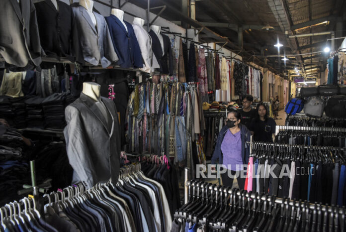 Pengunjung melihat pakaian bekas impor di salah satu kios. Presiden Joko Widodo menyatakan melarang bisnis pakaian bekas impor atau thrifting yang saat ini tengah populer di masyarakat karena mengganggu industri tekstil dalam negeri. Meski demikian, pedagang di pasar itu menolak larangan tersebut karena dinilai merugikan pedagang dan hilangnya pendapatan mereka.